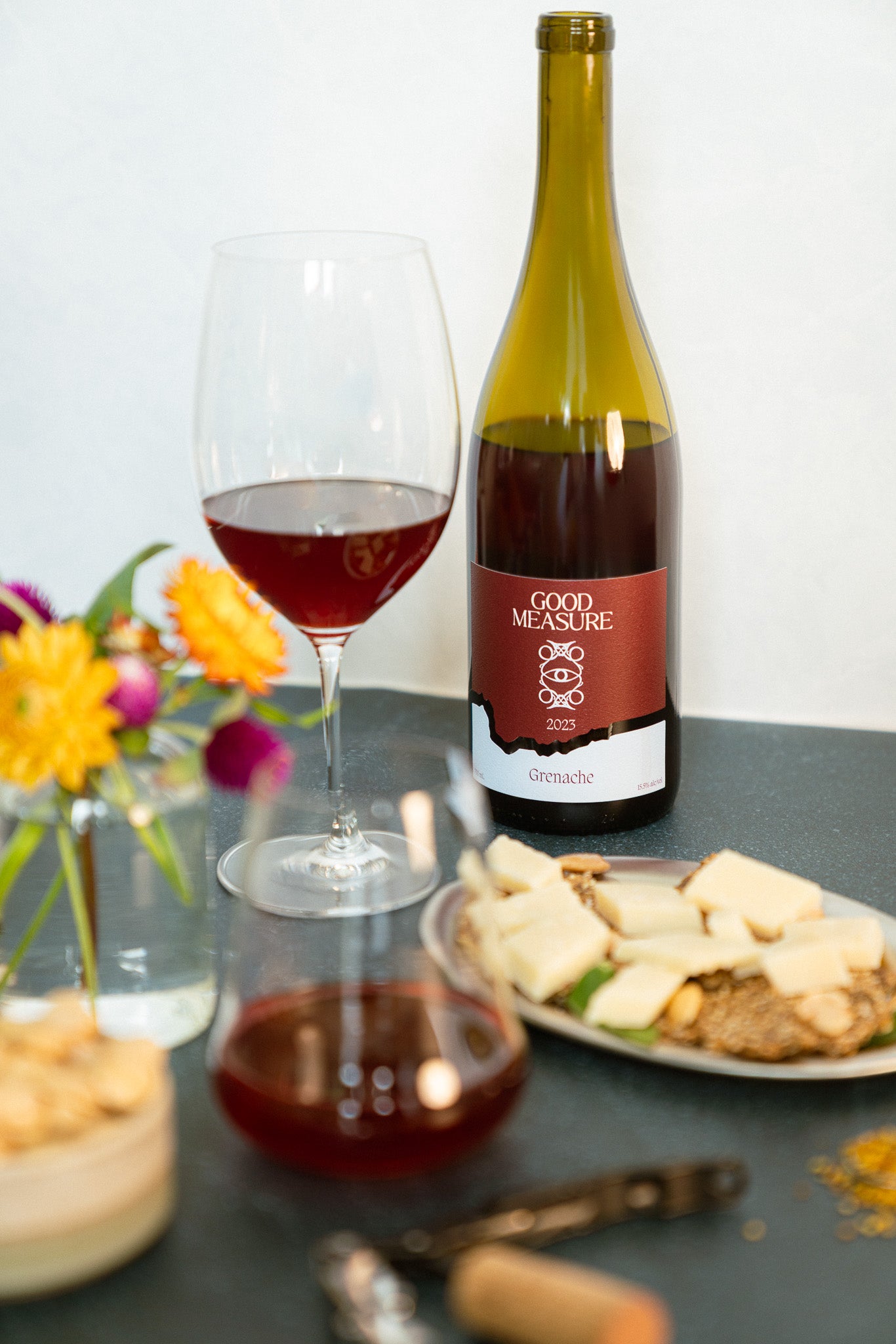 Bottle of Good Measure 2023 Oregon Grenache with burgundy and blue label next to glass and food